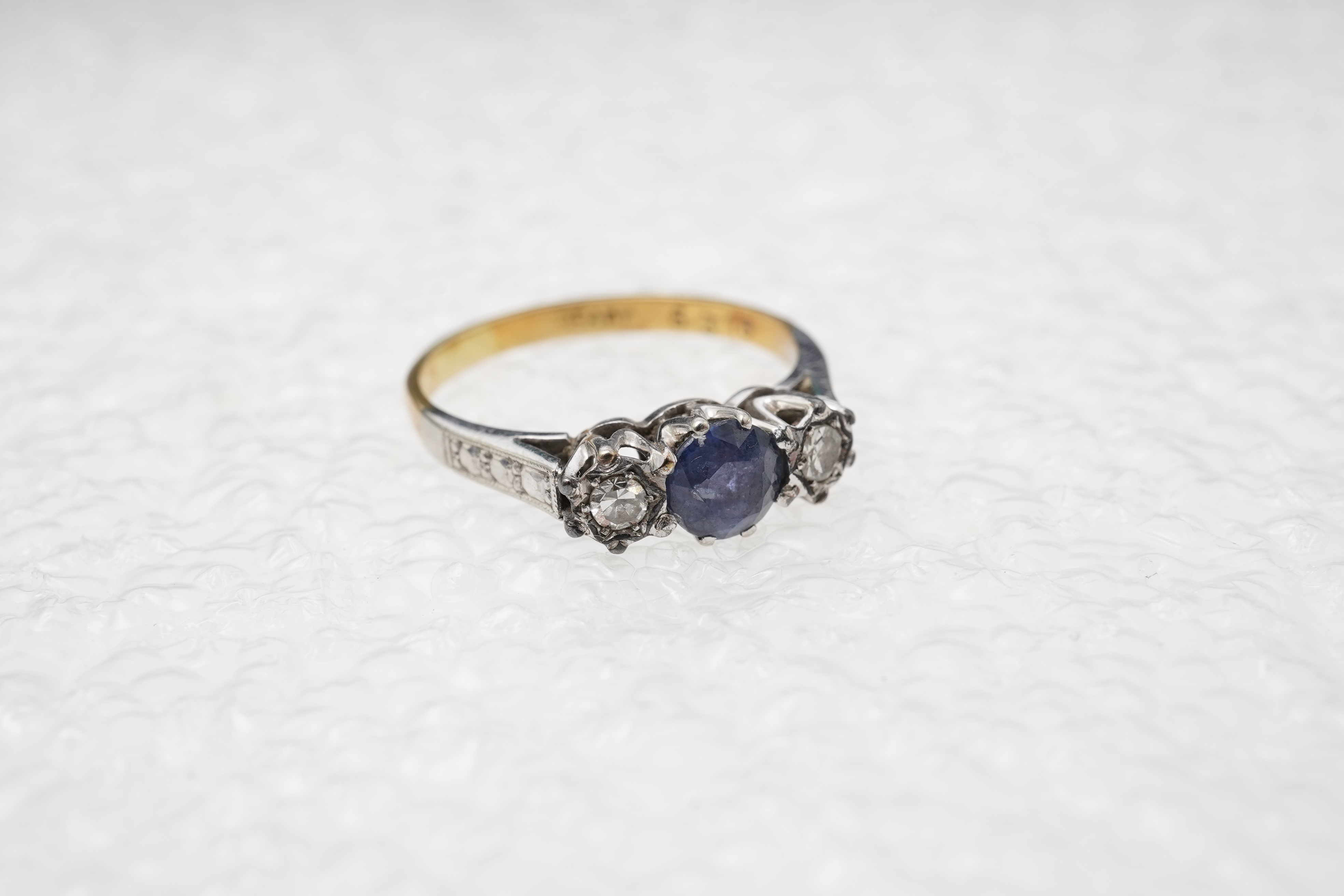 A sapphire and diamond three-stone ring, claw-set with a circular-cut sapphire measuring approximately 4.9 x 4.9 x 3.1mm, between single-cut diamonds totalling approximately 0.15 carats, mounted in gold and platinum, siz